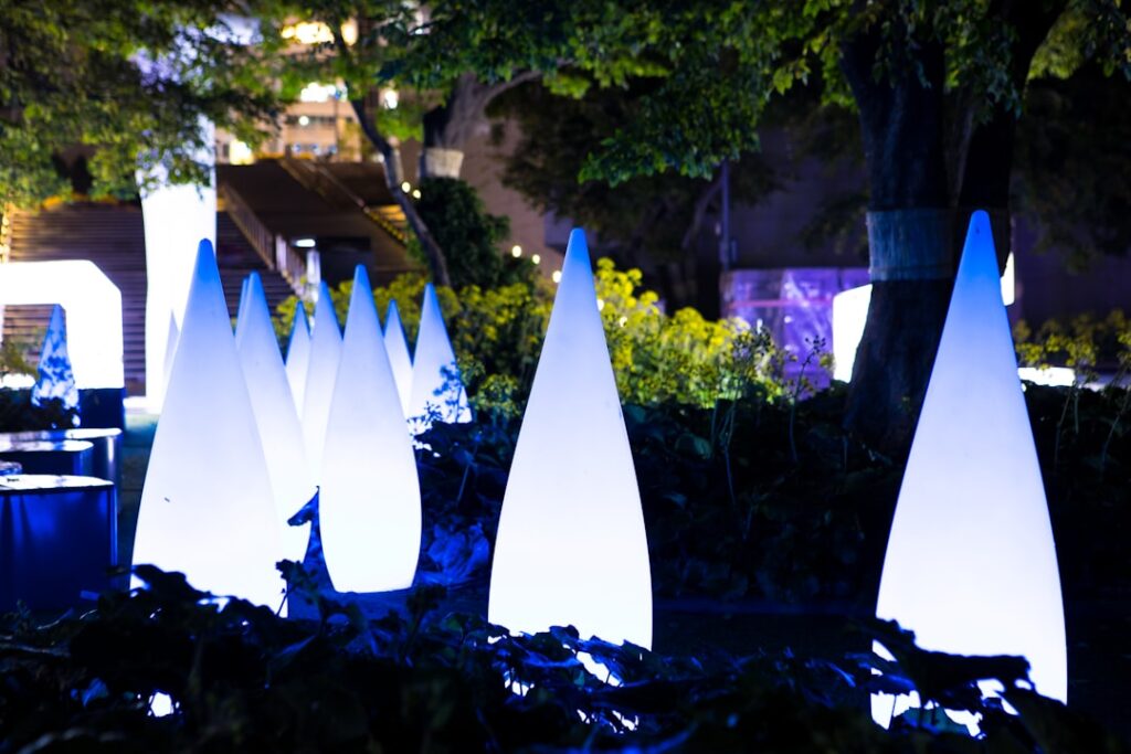Installazione notturna con coni luminosi blu in un giardino di Parma