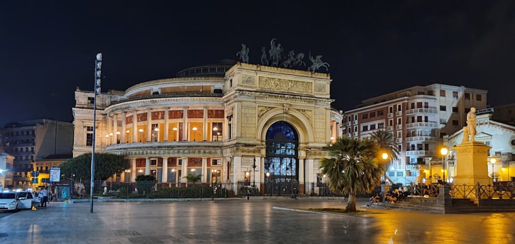 Teatro Regio di Parma illuminato nella piazza con statue e palme
