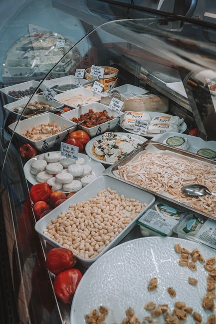 Glass deli case in Parma displaying cheeses, pasta, and antipasti trays.