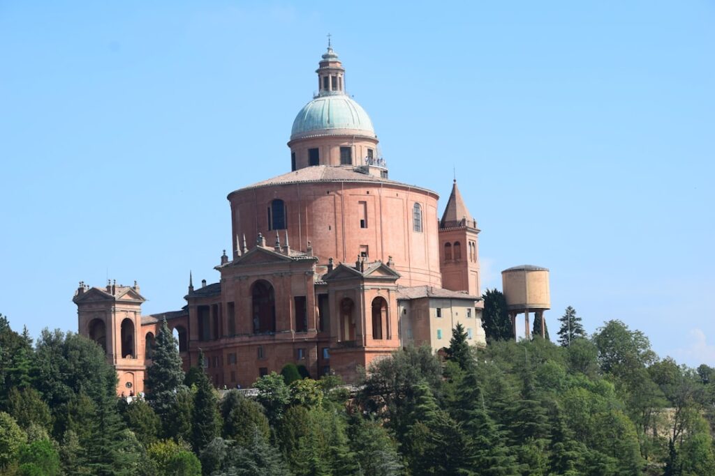 Rotunda z zieloną kopułą na wzgórzu nad Bolonią, otoczona drzewami
