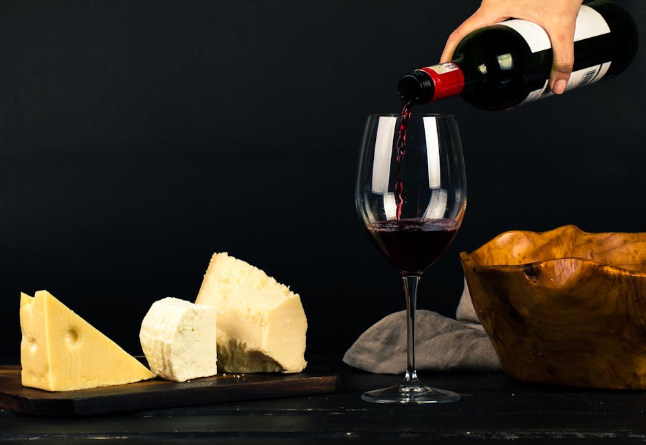 Red wine poured into glass beside assorted cheeses for Parma tasting