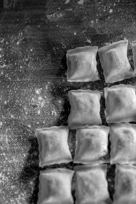 Black-and-white close-up of square stuffed pasta pieces dusted with flour