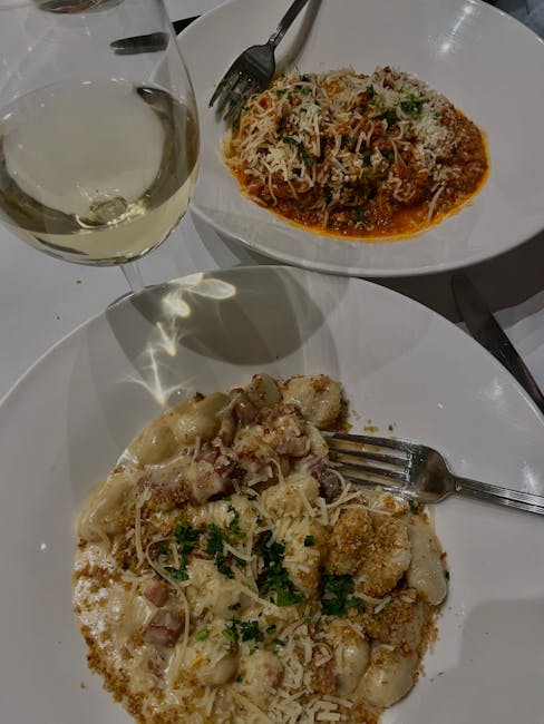 Due piatti di pasta con formaggio grattugiato e calice di vino bianco a Parma
