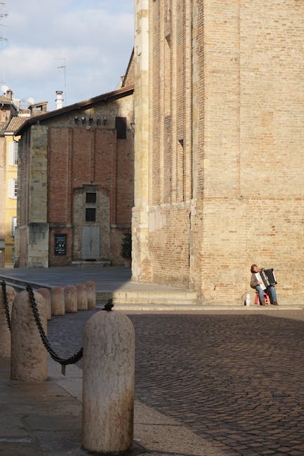 Musicista seduto con fisarmonica vicino alle mura di una chiesa a Parma