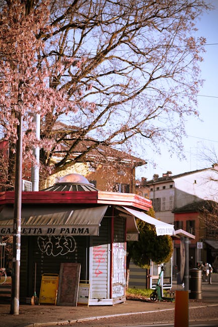 Chiosco con insegna Gazzetta di Parma sotto un albero in fiore