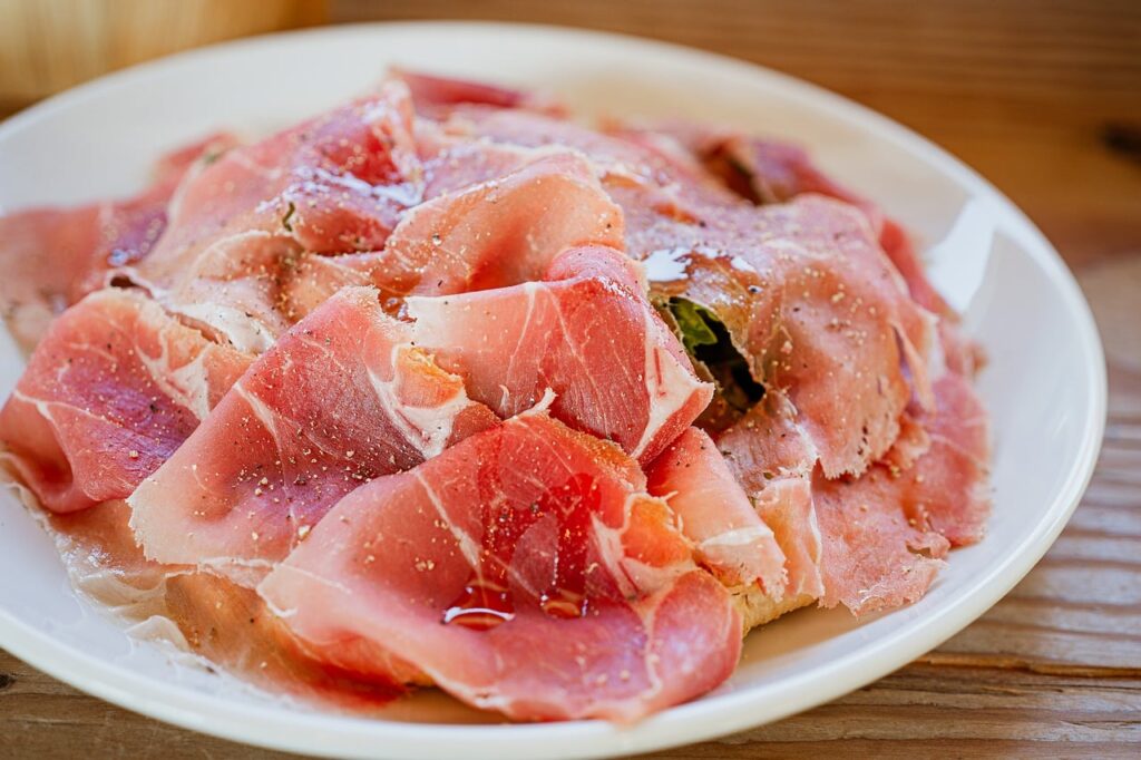 Plastry prosciutto di Parma ułożone na talerzu, skropione oliwą