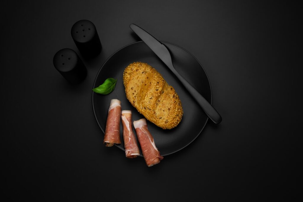 Schwarzer Teller mit Brötchen und Parmaschinken-Röllchen, stilvolle Anrichtung