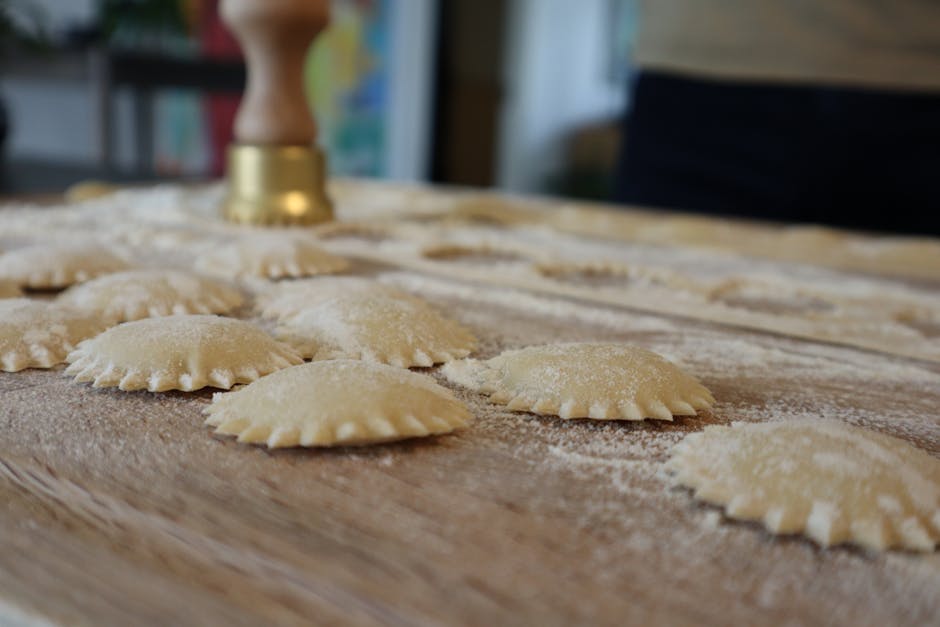 Rows of freshly formed ravioli dusted with flour on wooden board