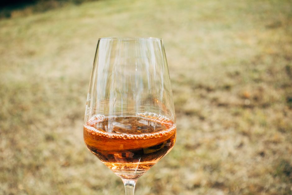 Glas Roséwein vor verschwommenem Grasfeld, leichte Perlage sichtbar