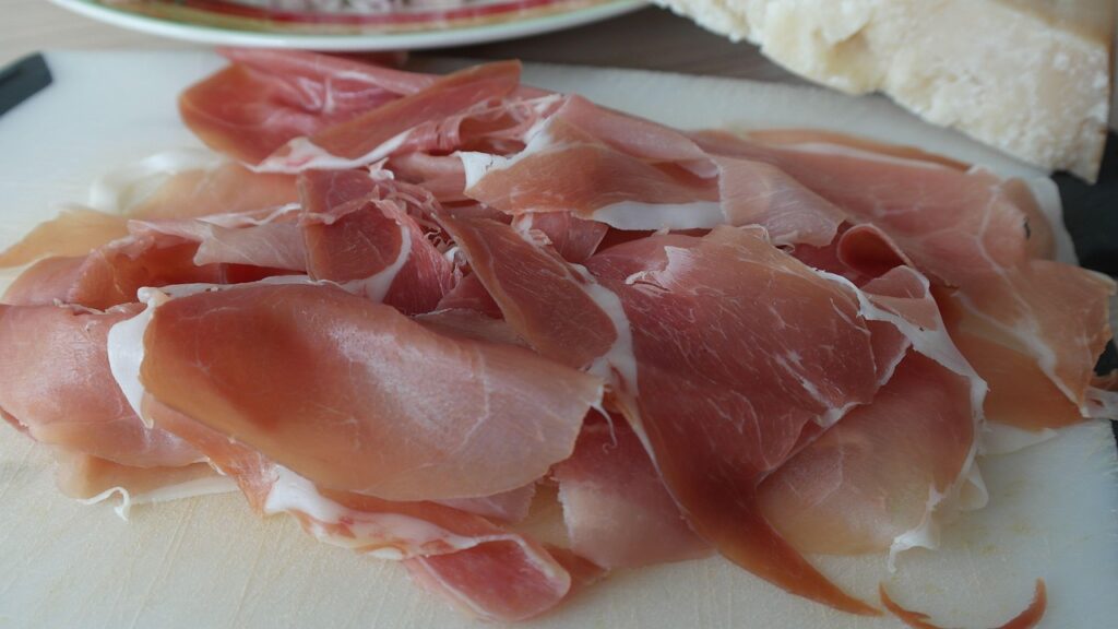 Plastry prosciutto parmeńskiego obok kawałka parmezanu
