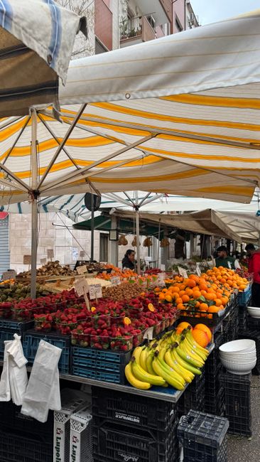 Striped yellow awning over crates of strawberries, bananas, and oranges at Parma market.