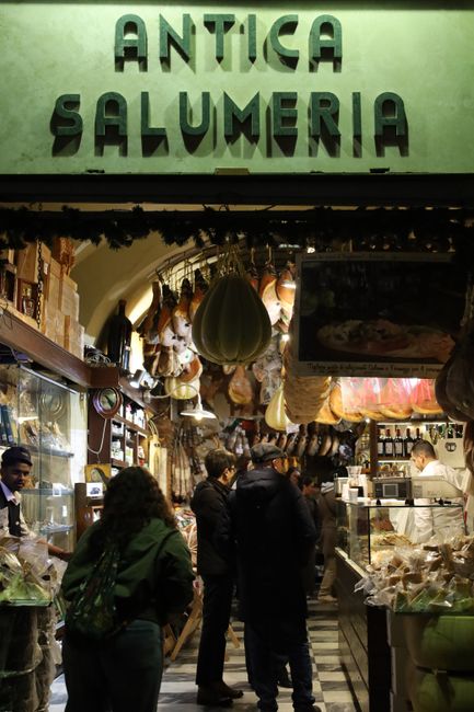Crowded Antica Salumeria entrance with hanging hams in Parma shop.