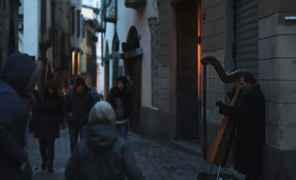 Musicien jouant de la harpe dans une ruelle animée de Bergame