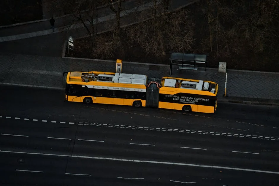Autobus articulé jaune garé près d'un arrêt vu de dessus.