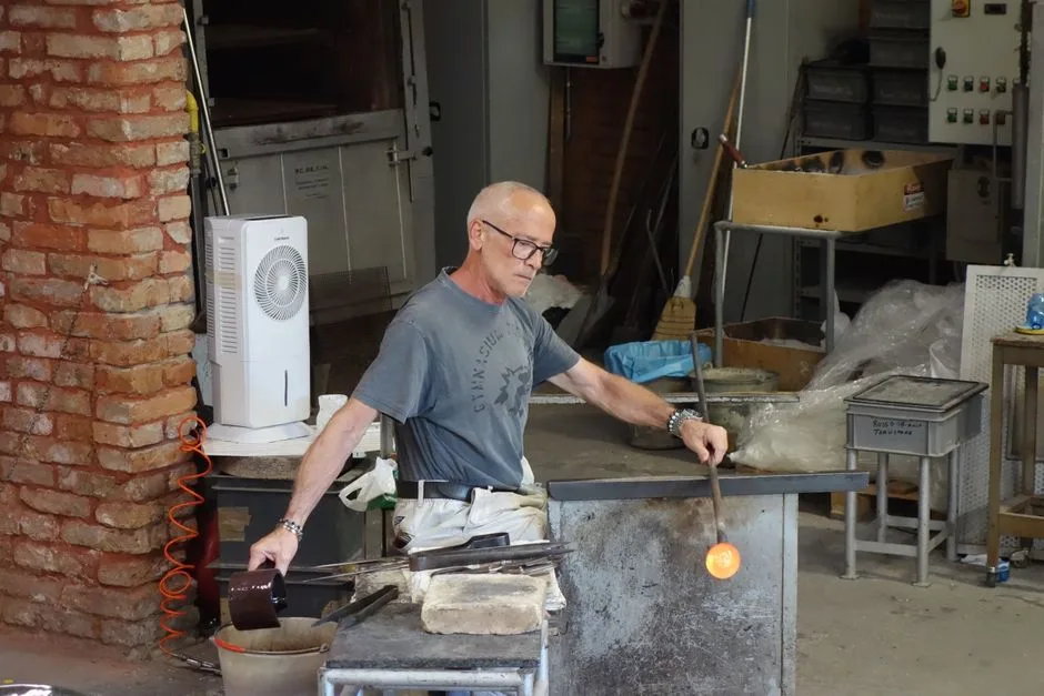 Verrier soufflant le verre chaud dans un atelier à Bergame