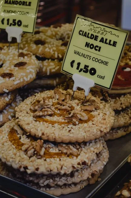 Biscuits aux noix empilés en vitrine, étiquette 'Cialde alle noci' à Bergame.