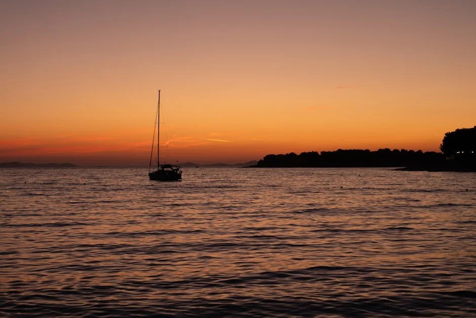 Sailboat silhouette at sunset off Trieste coastline over calm Adriatic waters