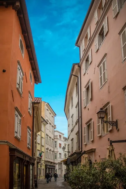 Allée piétonne bordée d'immeubles roses sous un ciel bleu à Trieste