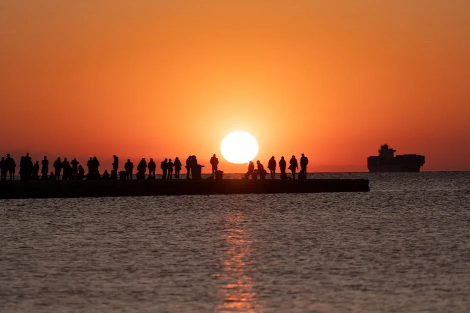 Silhouetted crowd on Trieste pier watching fiery sunset over Gulf