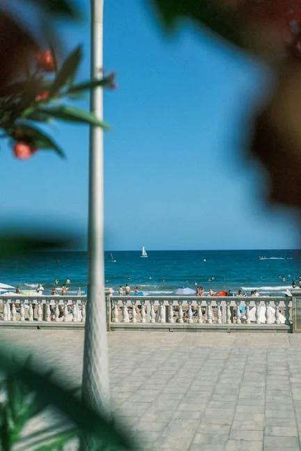 Vue sur la mer depuis la promenade, balustrade, baigneurs et voilier au loin