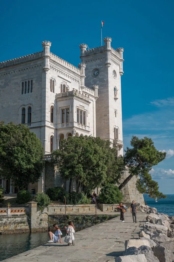 Visitors strolling the stone jetty beside Miramare Castle, Trieste.