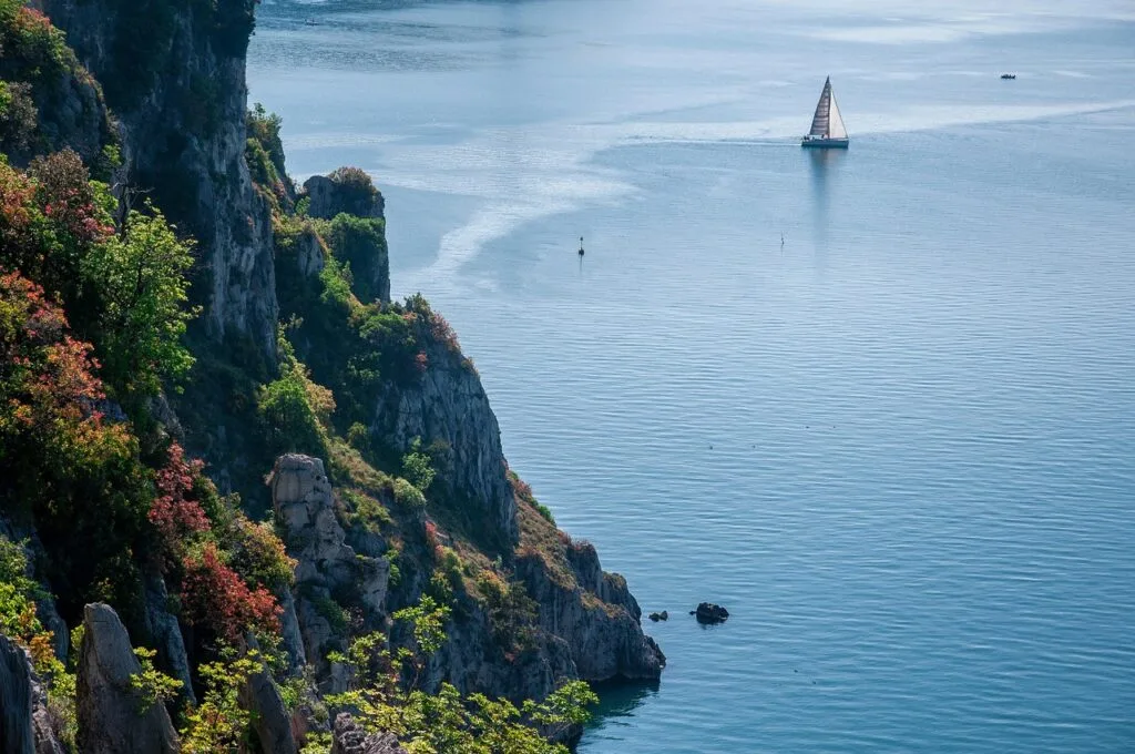 Falaises boisées plongeant vers la mer, voilier au large à Trieste.