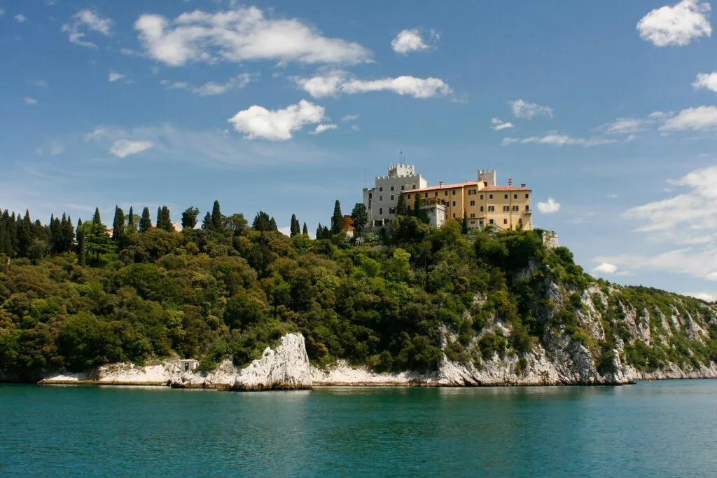 Château blanc et bâtiments jaunes sur promontoire boisé près de Trieste