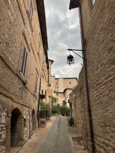 Ruelle étroite en pierre bordée de maisons anciennes, cloche suspendue.