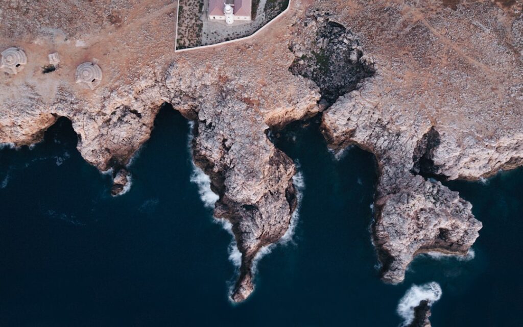Luftaufnahme zerklüfteter Küste mit Leuchtturm auf den Îles Éoliennes