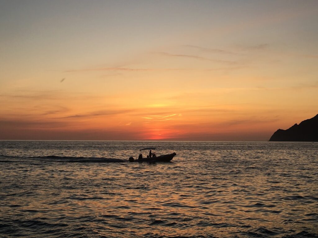 Silhouetted motorboat crossing sunset-lit sea off Îles Éoliennes coastline