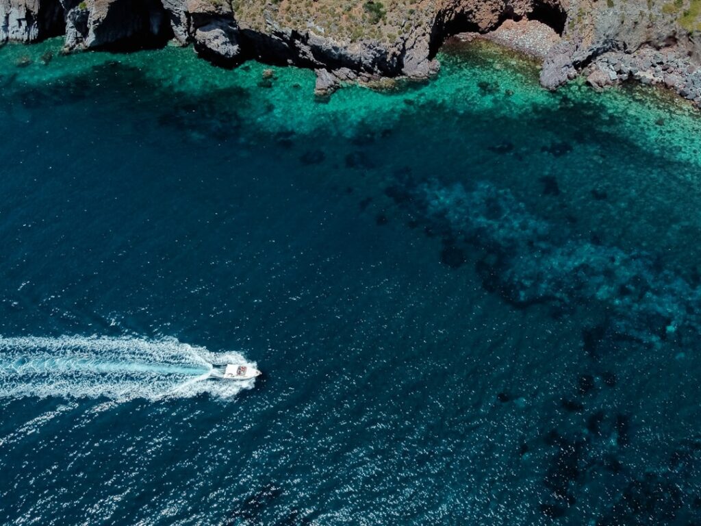 Barca che solca acque turchesi vicino costa rocciosa delle Isole Eolie