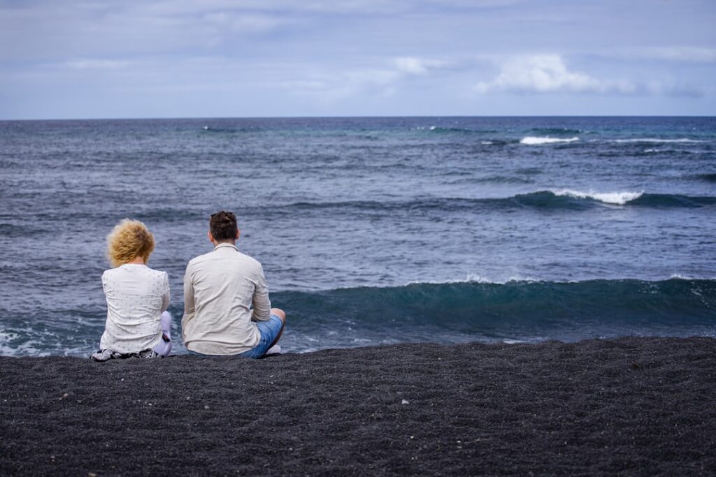 Couple assis sur la plage noire de Vulcano, regardant la mer