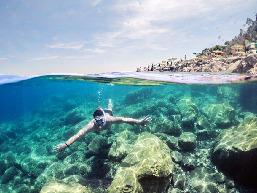 Snorkeler swimming above rocky seabed near Îles Éoliennes shoreline umbrellas