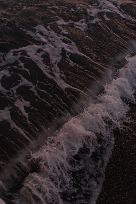 Onde che si infrangono su spiaggia scura delle Isole Eolie al crepuscolo
