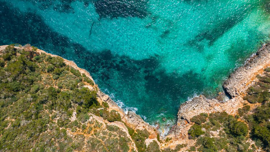 Aerial view of turquoise inlet and rocky cliffs in Îles Éoliennes