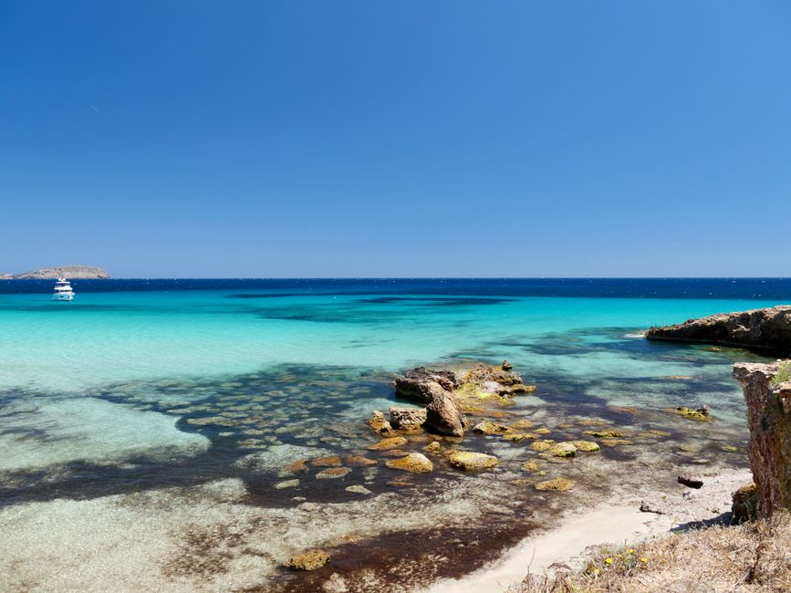 Turquoise shallow bay with rocky shoreline and boat off Îles Éoliennes coast