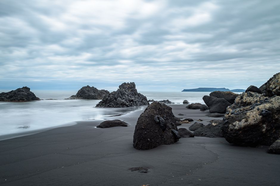 Black volcanic sand beach with jagged rocks under cloudy sky, Îles Éoliennes