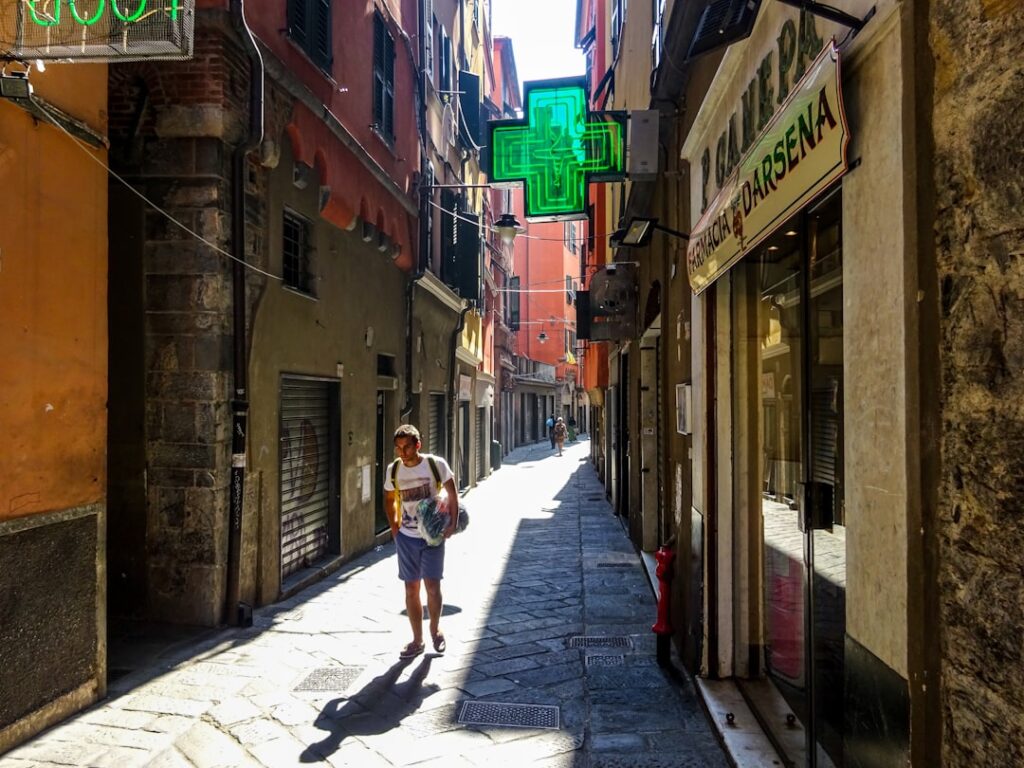 Ruelle étroite de Gênes avec enseigne de pharmacie verte et passant
