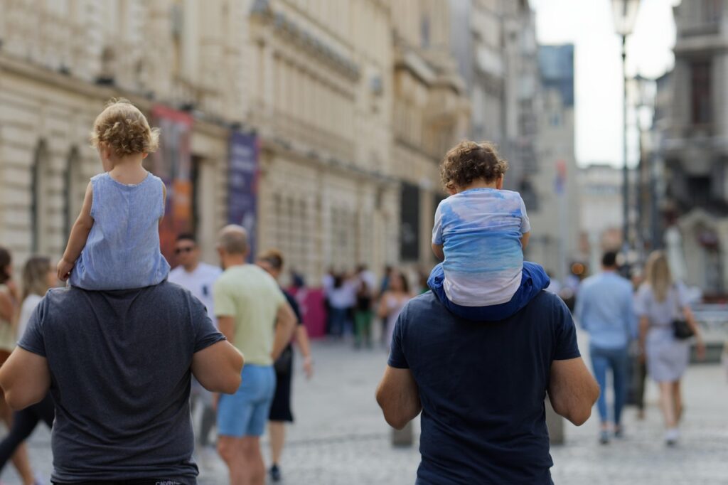 Twee kinderen op schouders van ouders wandelend door drukke straat in Ravenna