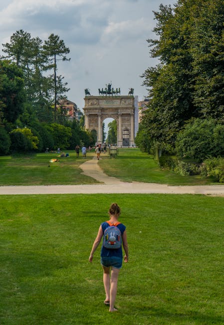 Osoba z plecakiem idąca po trawie ku łukowi w parku