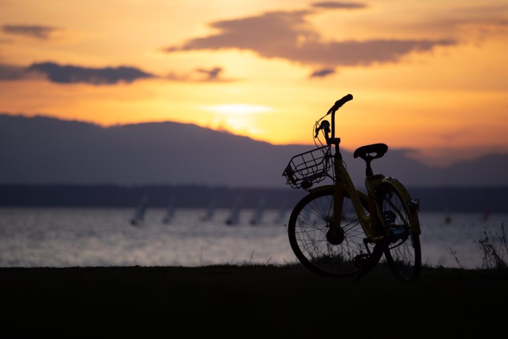 Vélo silhouetté au bord d'un lac au coucher de soleil, voiliers