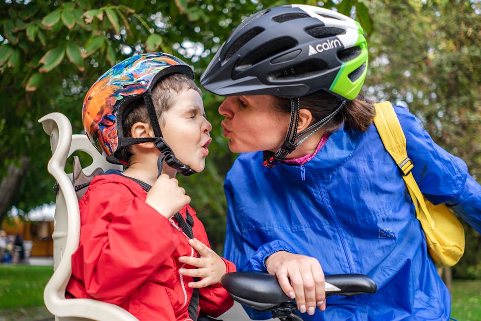 Eine Person mit Fahrradhelm küsst Kind im Kindersitz im Park