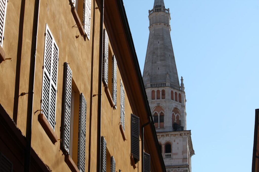 Ochre buildings framing Modena's Ghirlandina tower against clear sky