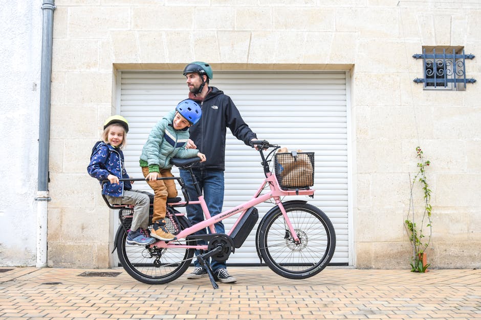 Padre con due bambini su cargo-bike rosa parcheggiata davanti