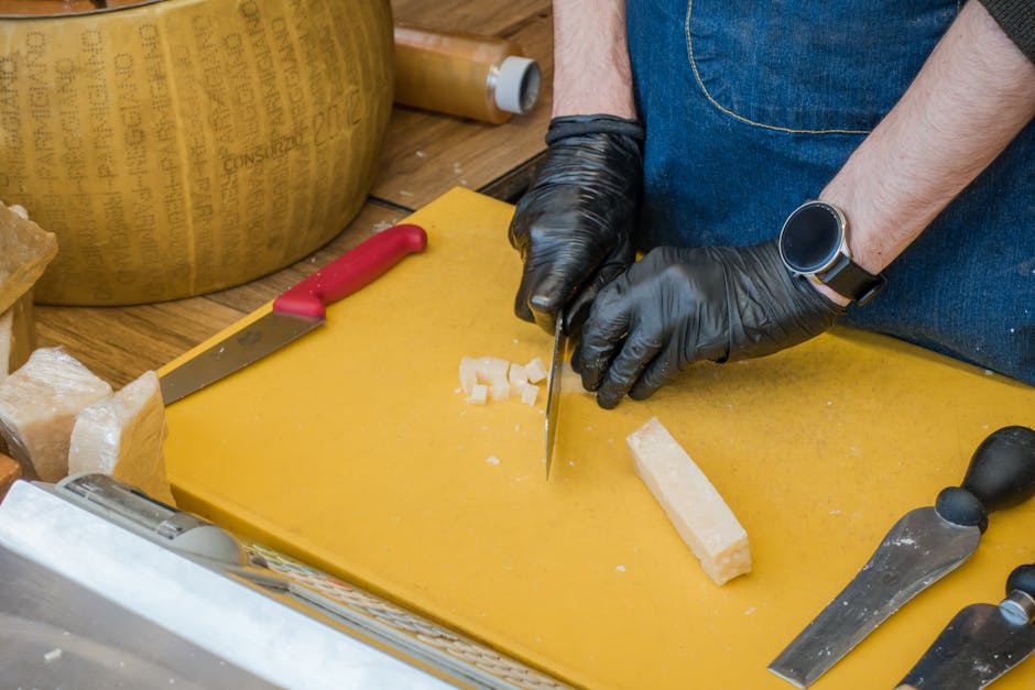 Handen met zwarte handschoenen snijden Parmigiano Reggiano blokjes op gele snijplank in Modena