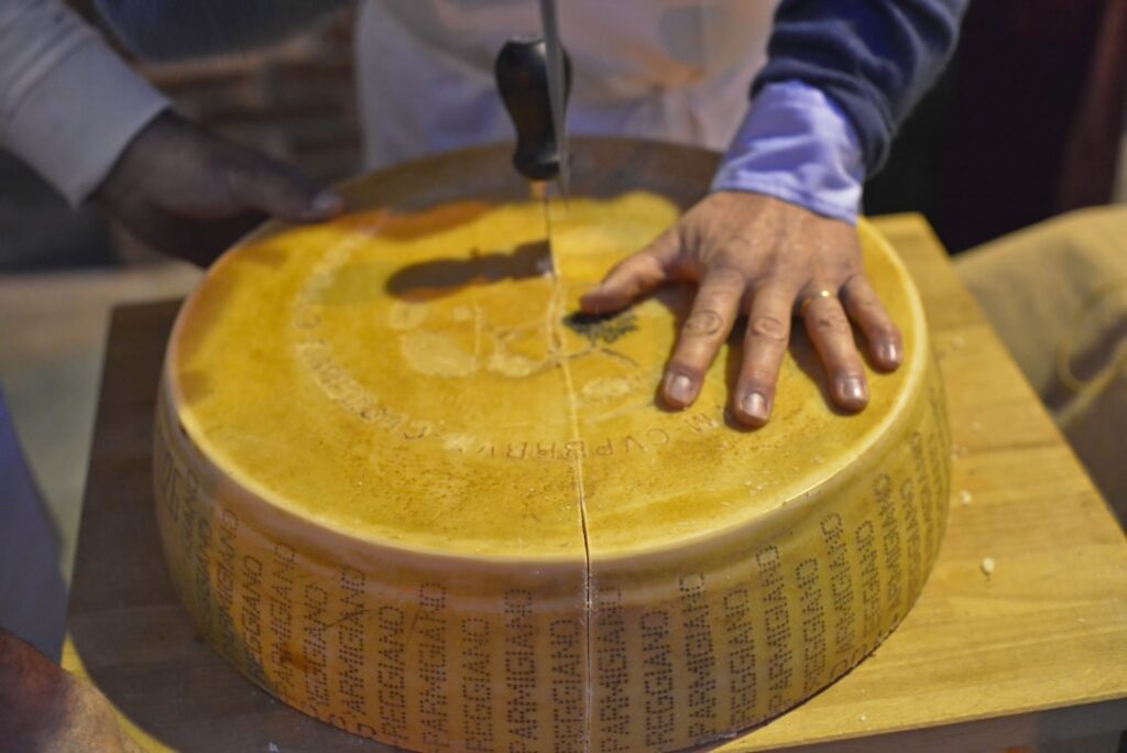 Mains coupant une meule de Parmigiano-Reggiano avec un couteau à Modène