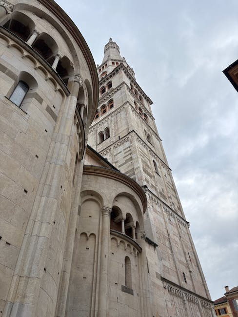 Ghirlandina bell tower rising above Modena cathedral's stone apse against cloudy sky