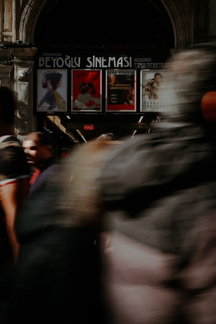 Passanti sfocati che attraversano un arco con locandine cinematografiche