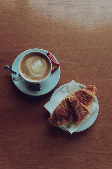 Kop cappuccino met lepeltje en croissant op houten tafel in Modena