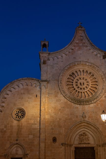 Ornate stone church facade with carved rose window at dusk.